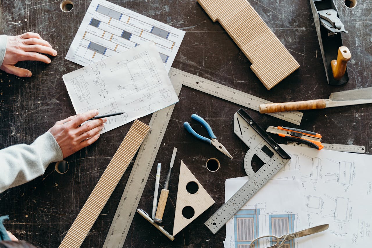 Tools and hands on a workbench during a woodworking project featuring plans and equipment.