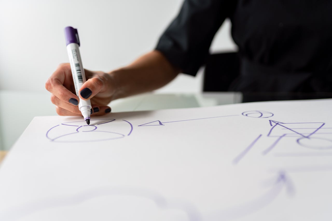A focused view of a hand drawing with a marker on a paper, capturing creative planning in progress.