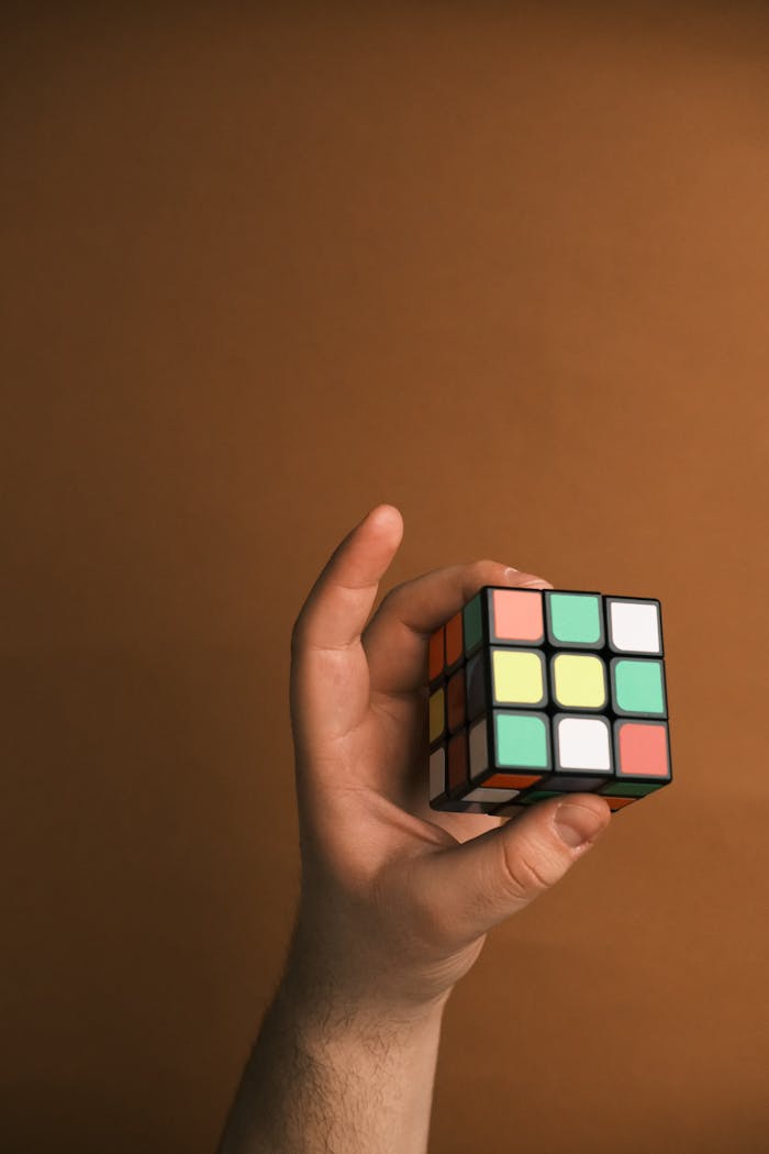 A hand holds a Rubiks Cube, showcasing strategy and intelligence against a brown backdrop.